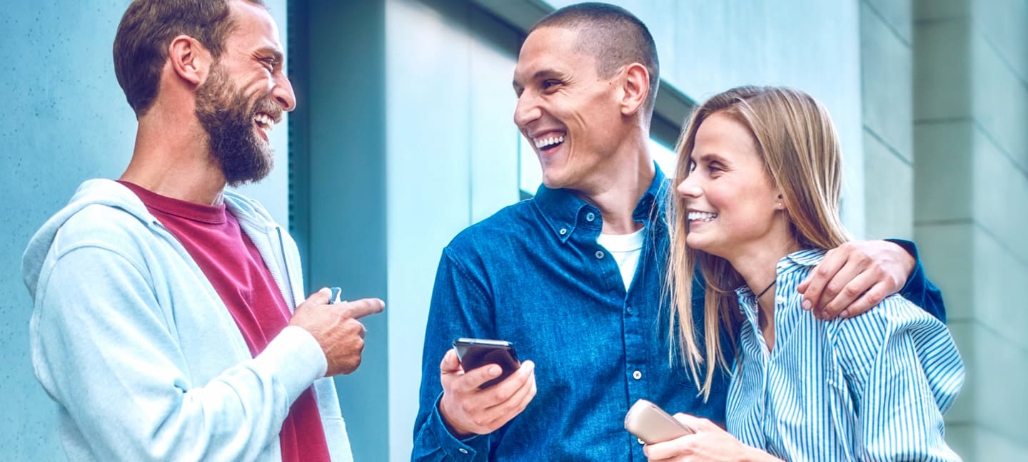 شخصان يحملان جهازي IQOS ILUMA يبتسمان بينما تنظر صديقتهما إلى تطبيق IQOS على هاتفها المحمول.